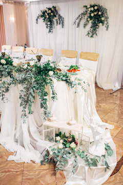 Decorative lanterns with green branches stand on the cloth hanging from dinner table