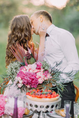 The close-up portrait of kissing bridesmaid and the best man behind the wedding table. The...
