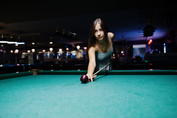 Portrait of an attractive young woman in dress playing pool.