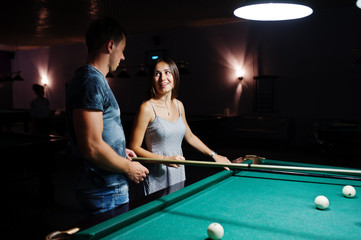 Fototapeta premium Woman in dress playing pool with a man in a pub.