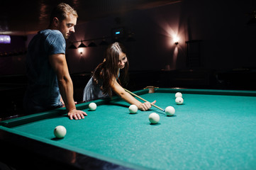 Woman in dress playing pool with a man in a pub.