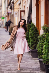 Woman in pink dress and beige coat walks along old street