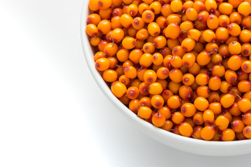 Part of a white plate filled with berries of sea-buckthorn on a white background. Right upper corner, top view.
