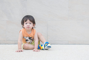 Closeup happy asian kid sit on marble stone floor and wall textured background with copy space
