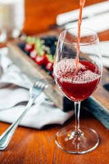 Pouring red wine into the glass against wooden background