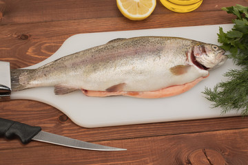 fresh trout fish on a cutting board with butter knife and spices