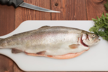 fresh trout fish on a cutting board with butter knife and spices
