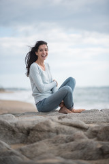 Fototapeta na wymiar A beautiful young brunette sitting on a rock at the beach