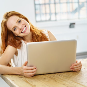 frau sitzt lächelnd am tisch mit ihrem notebook