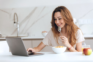 Obraz na płótnie Canvas Smiling woman using laptop while eating breakfast