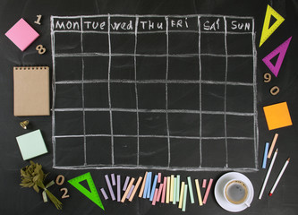 Grid timetable schedule with stationery on black chalkboard background.