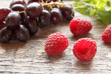 Berries of ripe raspberry and black grapes on a wooden background. Selective focus.