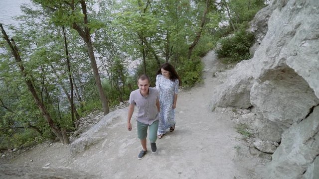 The guy and the girl are walking along the cliff. A loving couple kisses near a stone precipice.