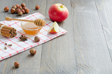 Bowl of honey, honey stick, cinnamon, hazelnuts and red apple