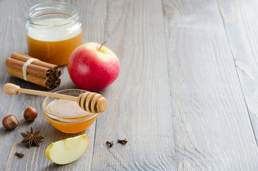 Bowl of honey, honey stick, cinnamon, hazelnuts and red apple