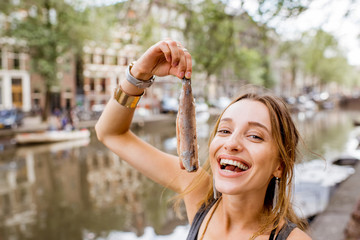 Naklejka premium Młoda kobieta jedzenie świeżego harringa stojącego na zewnątrz w mieście Amsterdam. Harring z cebulą to tradycyjna holenderska przekąska