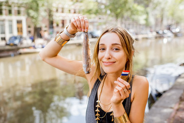 Obraz premium Młoda kobieta trzyma świeżego harringa stojącego na zewnątrz w mieście Amsterdam. Harring z cebulą to tradycyjna holenderska przekąska