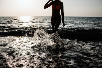 Backlit shot of the girl running with her legs in the water at the beach on a Sunny day in the summer. water splashes