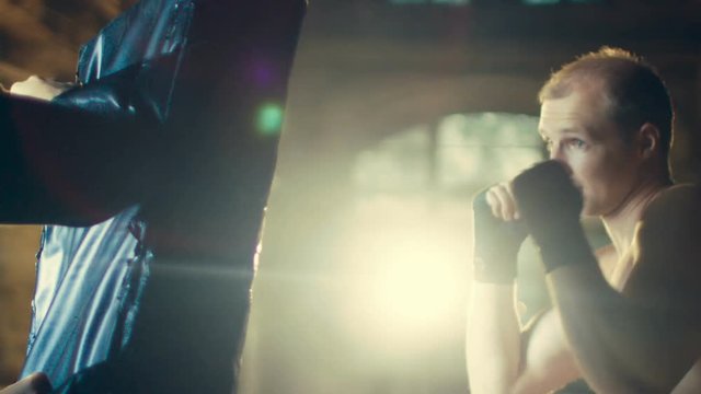 Muscular Man Trains His Punches with a Punching Bag that His Partner/ Trainer Holds. He's Professional Figher and It's Part of His Fight Preparation Training/ Exercise. 