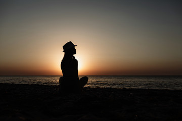 Beautiful girl in a red hat smiling at the summer waterfront. Silhouetted photo in the sunlights at sunset.