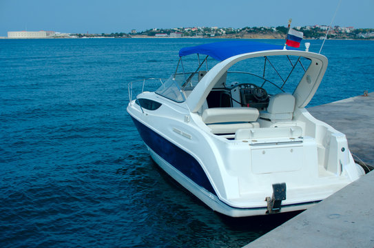 A modern boat of white color with the flag of Russia stands at the pier in the bay.