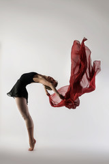 graceful ballet dancer dancing on a light background with a fluid, lightweight red cloth