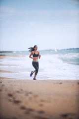 Beautiful young woman in sportswear runs on the beach