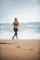 Beautiful young woman in sportswear runs on the beach