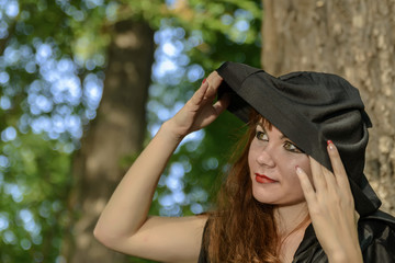 young pretty girl in a Gothic style takes off a black hood in a beautiful forest