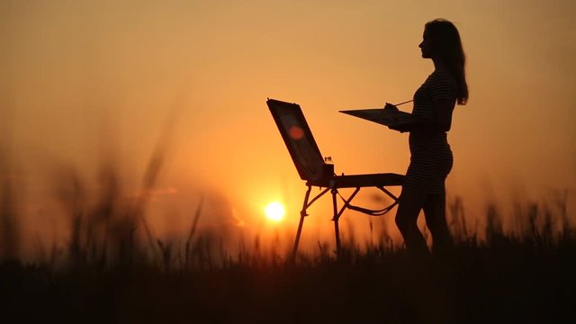Young girl draws an image in the field at sunset. Creativity and inspiration.