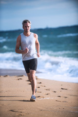 Gray haired man in sportswear runs on the beach