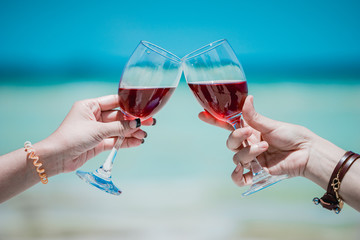 Young Asian woman wearing Hawaiian with hat and sunglasses is happy when they go to the beach for a holiday. Drinking a glass of wine together.
