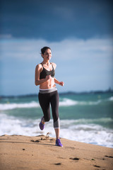 Beautiful young woman in sportswear runs on the beach