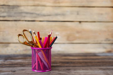 Scissors and colorful pencils of violet yellow pink red and orange in stationary cup on wooden table and background. Copyspace school concept