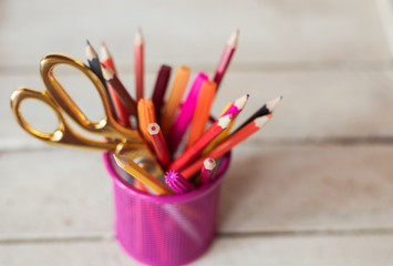 Scissors and colorful pencils of violet yellow pink red and orange in stationary cup on wooden table and white background. Copyspace school concept