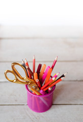 Scissors and colorful pencils of violet yellow pink red and orange in stationary cup on wooden table and white background. Copyspace school concept
