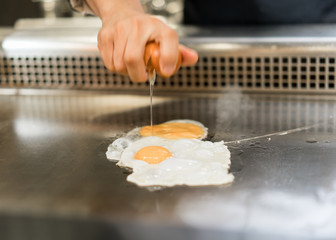 Hand of Chef cooking egg on hot pan in front of customers.