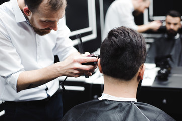 Fototapeta premium Master cuts hair and beard of men in the barbershop, hairdresser makes hairstyle for a young man