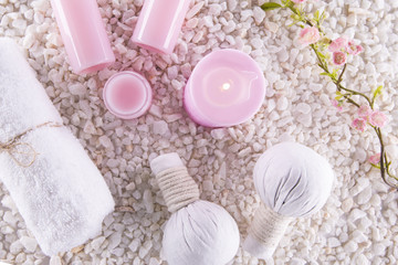 Fototapeta na wymiar Spa. Still life. Candle, bottles with cream of pink color, a towel and flowers on a background of white pebbles. Top view