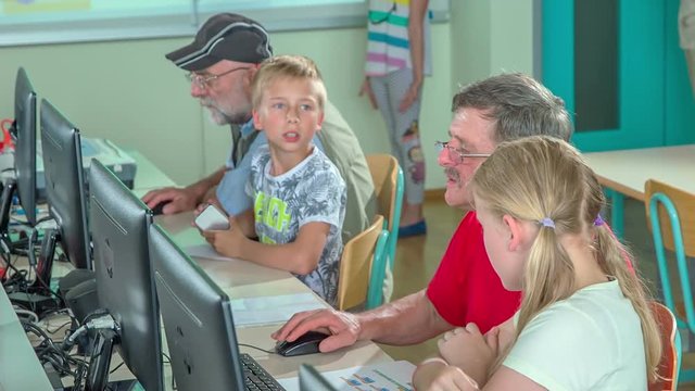 Kids and their grandparents are learning some computer basics together in a computer lounge.