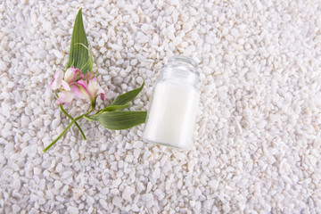 Spa. Still life. Altromeria and bottle with cream on a background of white pebbles.