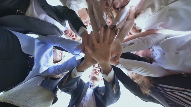 College Students Teamwork Stacking Hand Concept. Friendly graduates of the senior school put their hands on each other and open them against the white sky. Sunny daylight