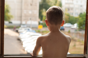 A lonely little boy looking through the window,