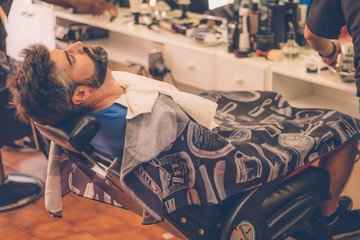 Man with beard sitting on the chair at barbershop.