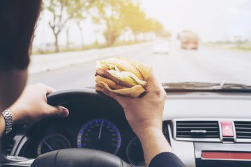 Man driving car while eating hamburger