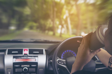 Lady driving car while holding a cup of coffee