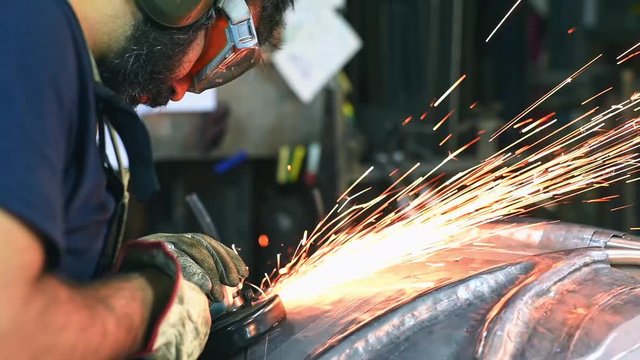 Steel worker polishing metal surface in workshop