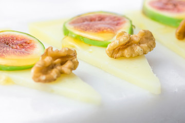 Slices of cured semi-hard Spanish goat cheese with walnuts, ripe figs drizzled with honey on white marble serving board. Appetizer, gourmet concept. Mediterranian cuisine. Copy space.