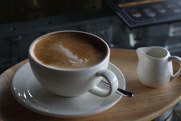 Latte coffee in a white glass placed on a wooden tray is served in the morning at a coffee shop.