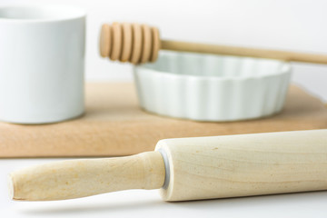 Wooden rolling pin, white measuring cup, baking form and honey dipper on cutting board. White tabletop background. Clean minimalist styled image. Template for menu, banner, card. Copy space.